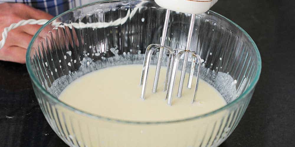 A hand mixer in a large bowl of lemon ricotta pancake batter.