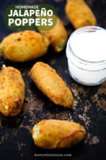 5 jalapeño poppers on a scratchy baking sheet next to a small jar of sour cream.