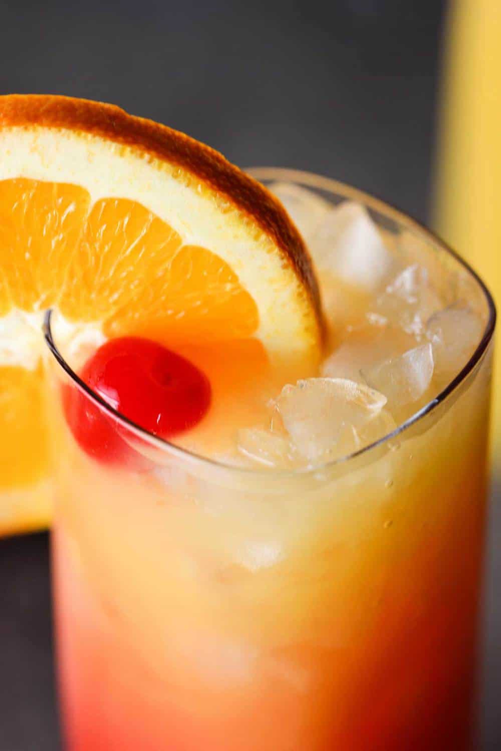 Close up shot of a tequila sunrise with a large wagon wheel orange garnish on the glass.
