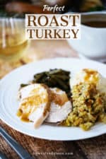 A white gravy boat pouring turkey gravy over a plate of mashed potatoes, dressing, turkey, and green beans.