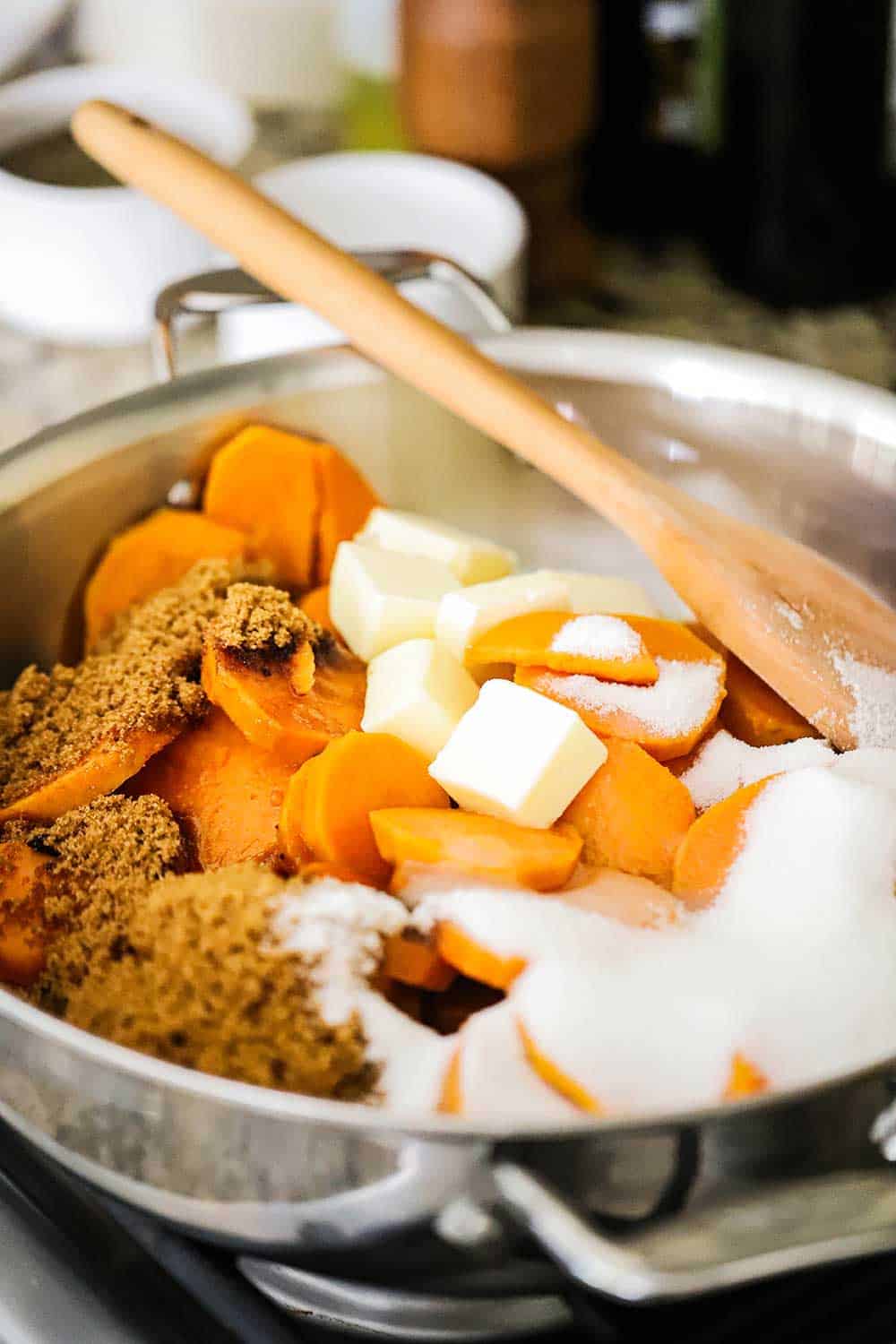 A large saucepan filled with sliced sweet potatoes, brown and white sugar, and sliced pieces of butter.