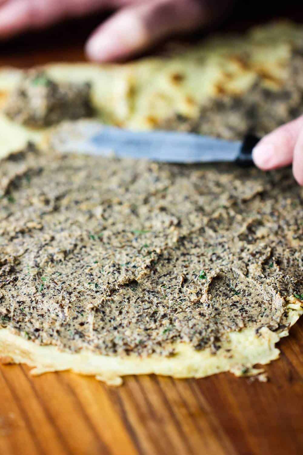 Knife smearing filling on crepes for beef Wellington