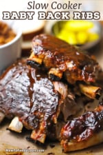 Two half-racks of slow cooker baby back ribs stacked on top of each other and with barbecue sauce smear over the tops of each rack.