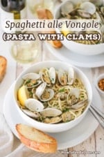 An overhead view of a white pasta bowl filled with a serving of spaghetti alle vongole with clams in their shell sitting on top and piece of toasted bread next to the bowl.