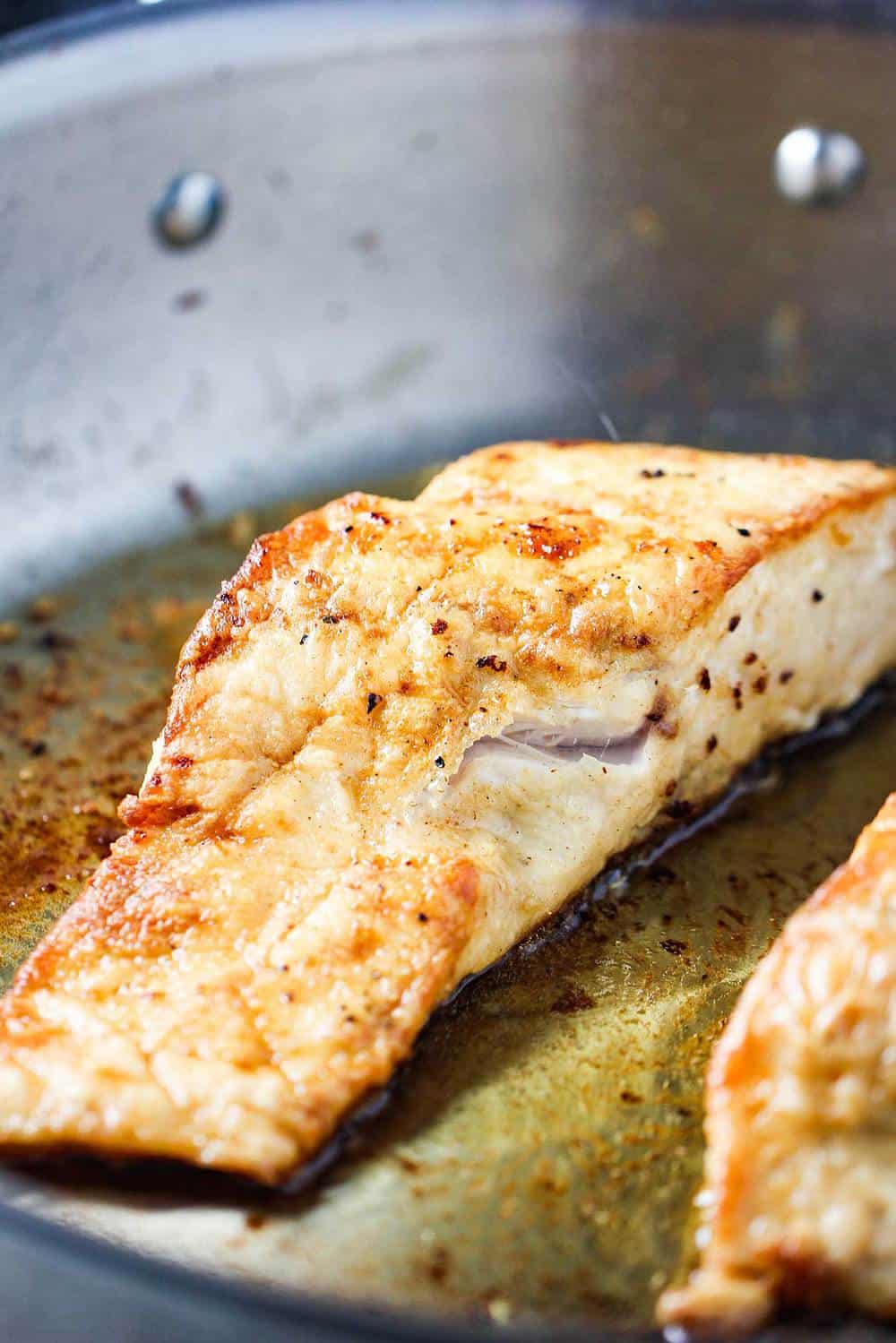 Wild striped bass being seared in a large skillet with olive oil.