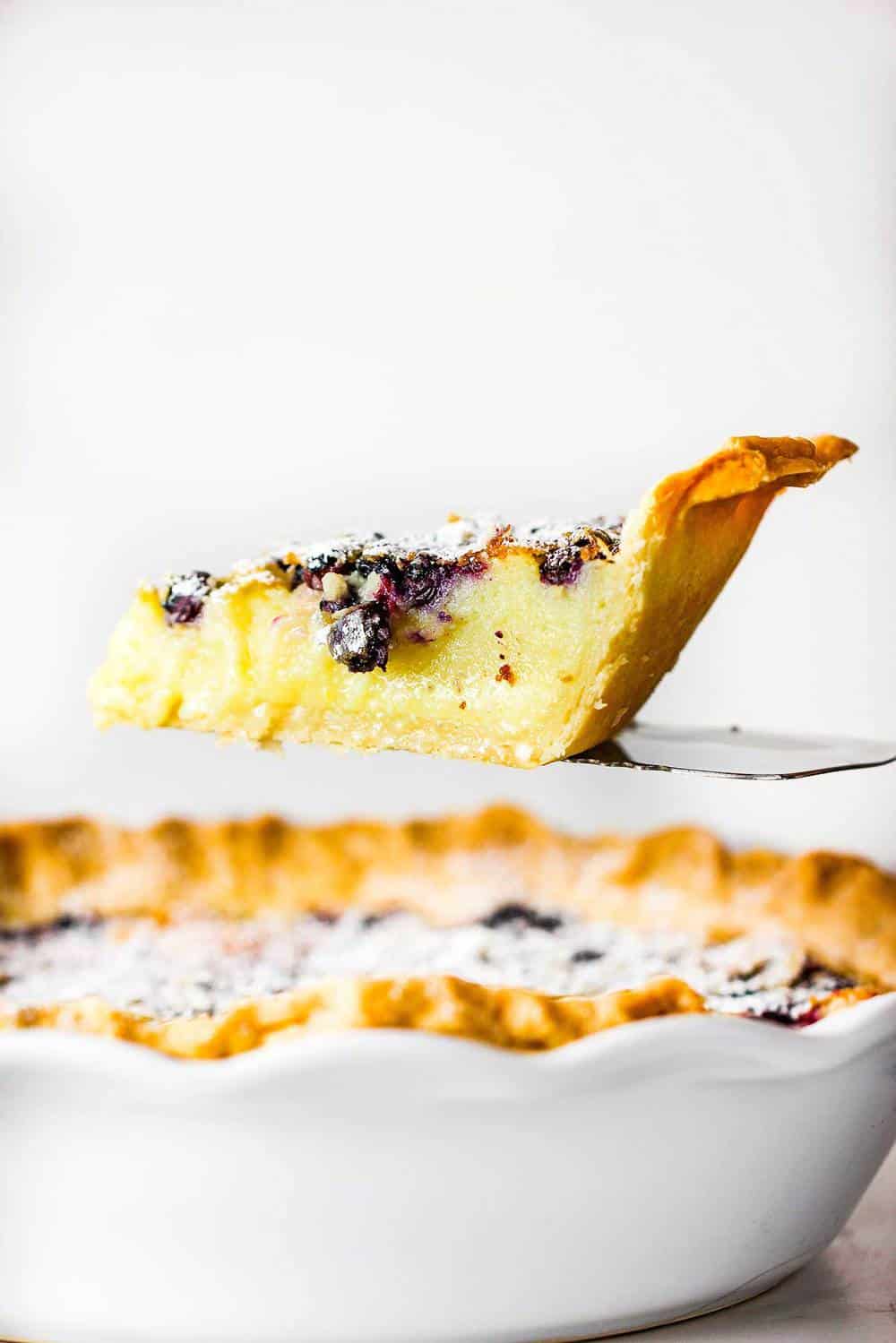 A slice of blueberry buttermilk pie being lifted from the pie on a spatula.