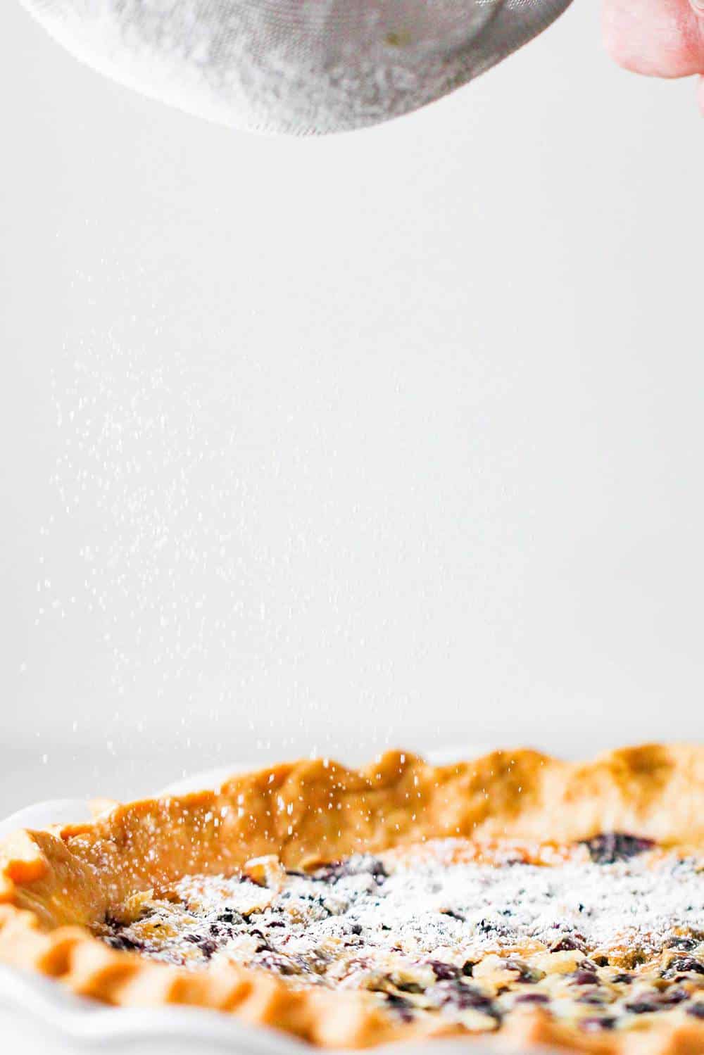 Powdered sugar sprinkling onto a blueberry buttermilk pie.