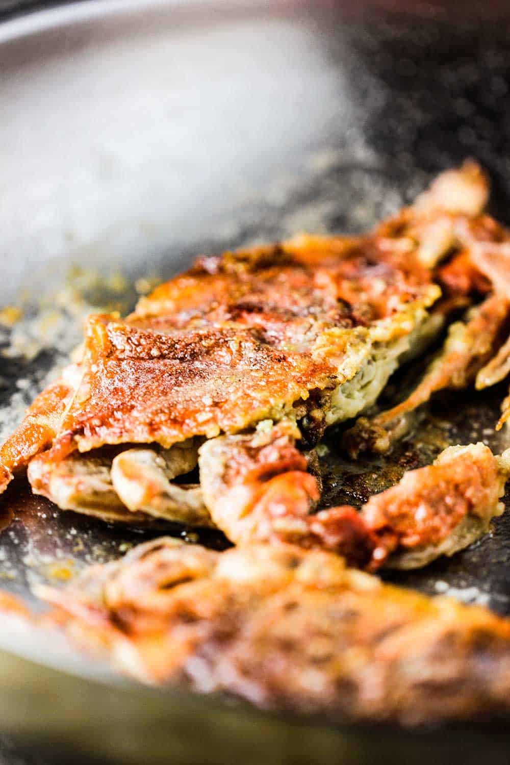A close-up view of two sautéed soft-shell crabs in a skillet.