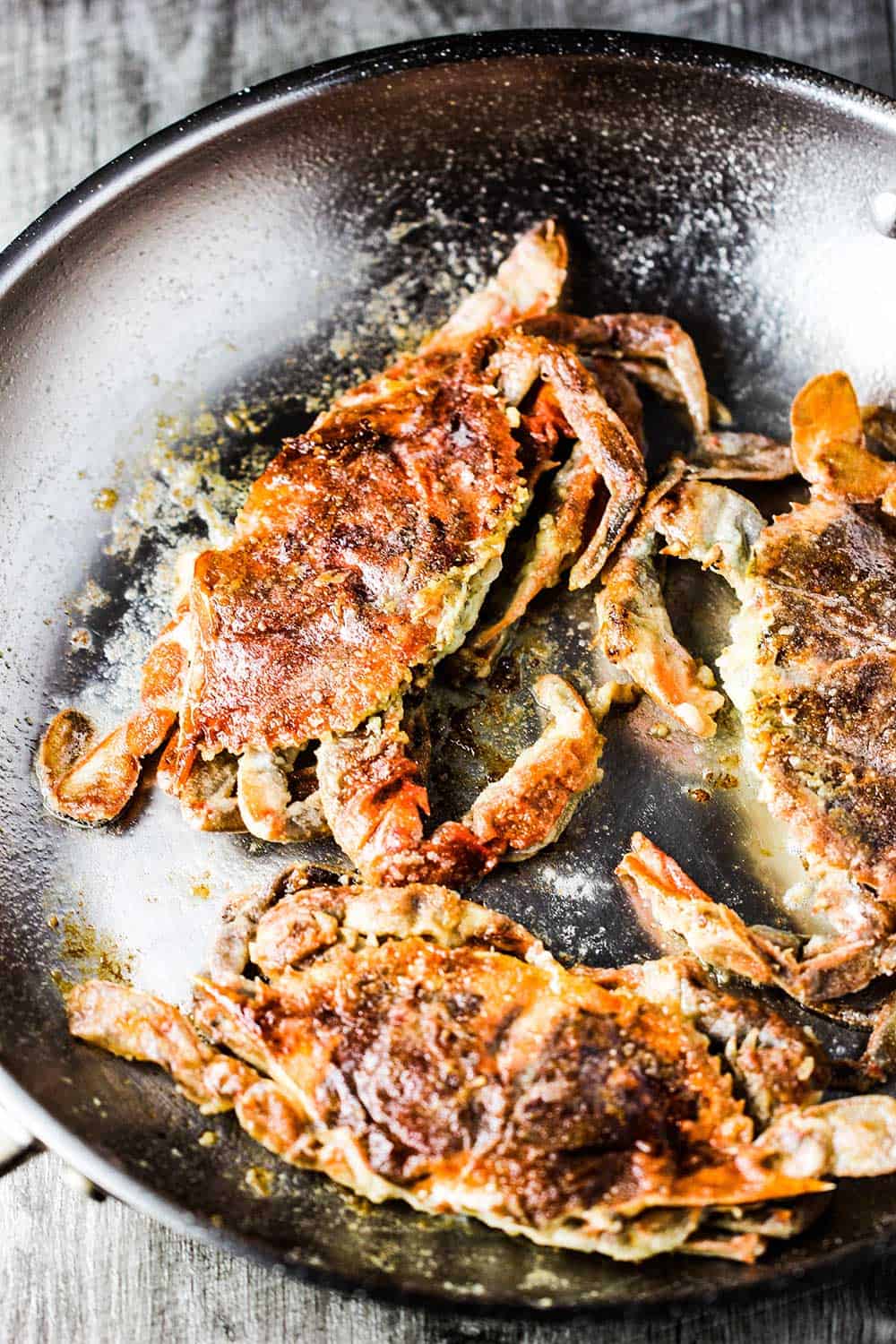 Three sautéed soft-shell crabs in a silver skillet.