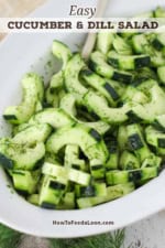A white oval serving dish filled with sliced cucumber and dill salad with sprigs of fresh dill in front of the bowl.