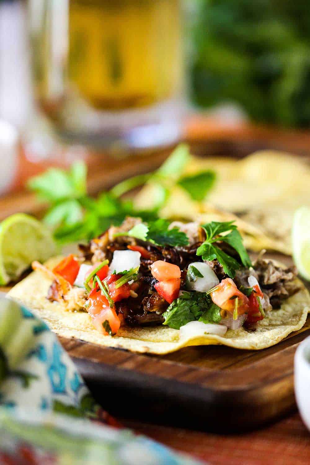 Pork carnitas tacos with traditional garnishes and a glass of beer.