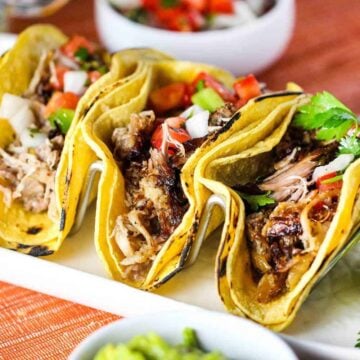 A white platter with three Carnitas Tacos