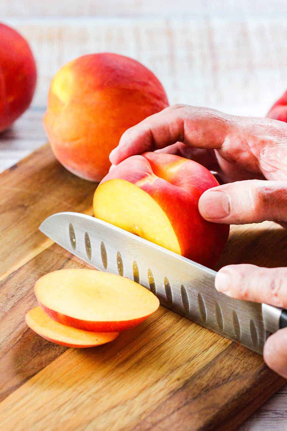 A chef's knife slicing through a yellow peach.