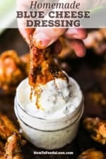 A person plunging a grilled buffalo wing into a small glass jar filled with homemade blue cheese dressing.