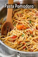 A large silver saucepan filled with homemade pasta pomodoro with a wooden spoon in the pan.