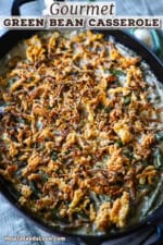 A straight-on view of a large oval baking dish that is filled with gourmet green bean casserole and topped with fried onion strips.