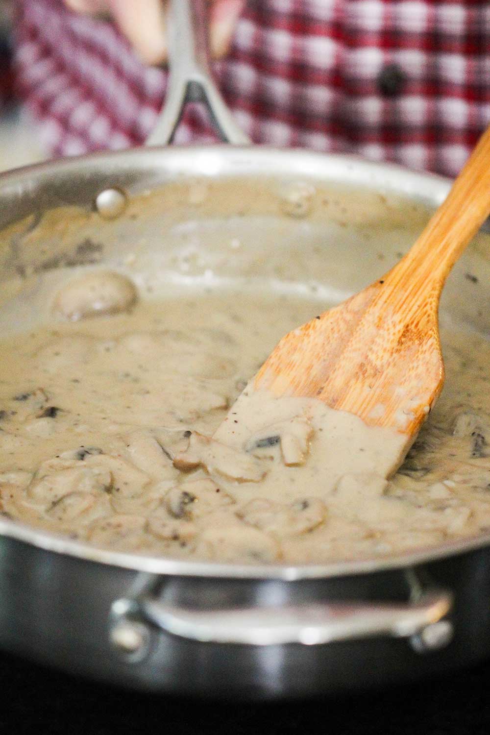 A large steel skillet holding a mushroom sauce with a wooden spoon in it.