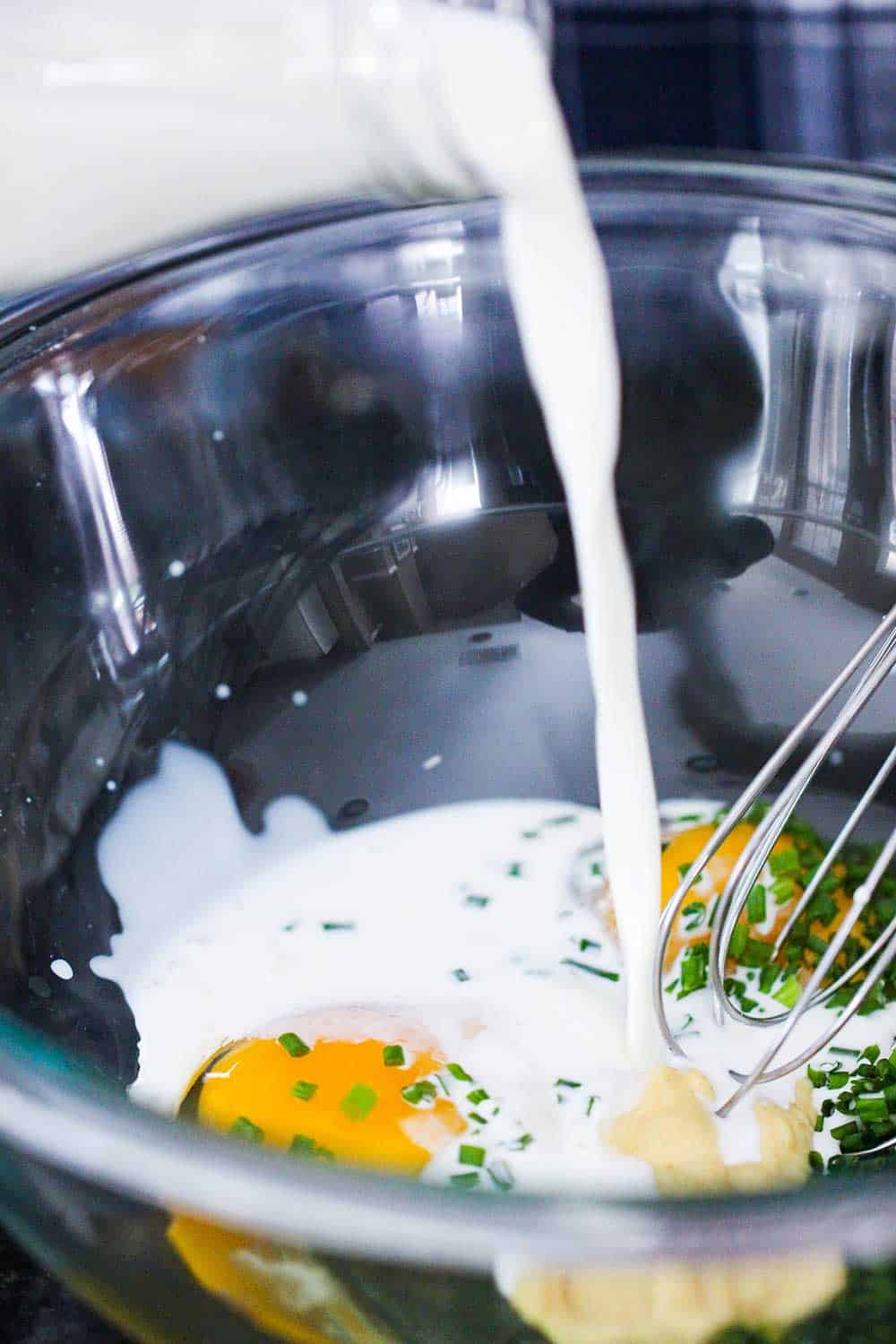 Cream being pour into a glass bowl filled with eggs, chives and Dijon mustard.