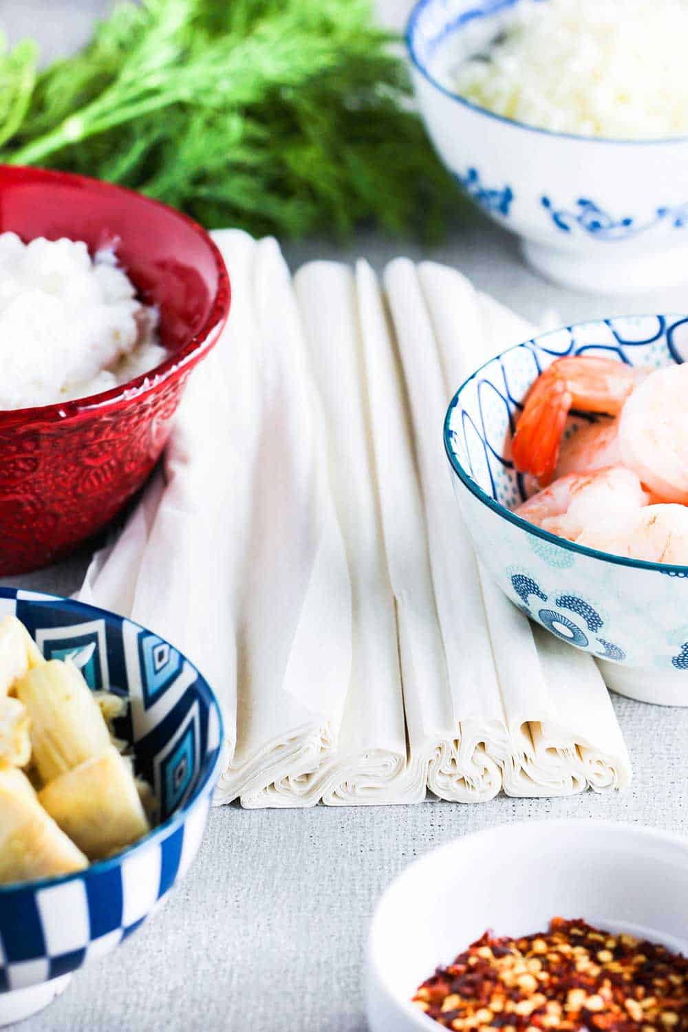 A bowl of artichoke hearts next to a bowl of ricotta cheese, and a bowl of shrimp cocktail between sheets of phyllo dough.