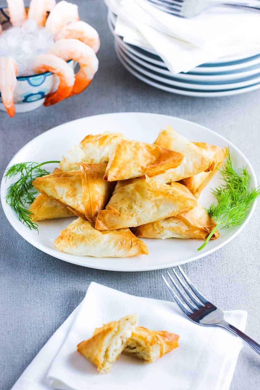A white plate holding air fryer phyllo triangles next to shrimp cocktail.