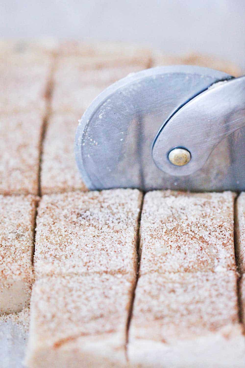 A pizza cutter slicing square of snickerdoodle fudge.