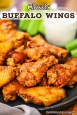 A close-up view of classic Buffalo wings on a black plater with a jar of blue cheese dressing in the background.