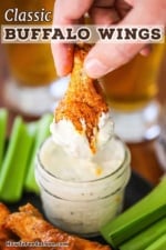A person holding an Italian-style chicken wing that has been plunged and removed from a yellow bowl of gorgonzola dipping sauce.
