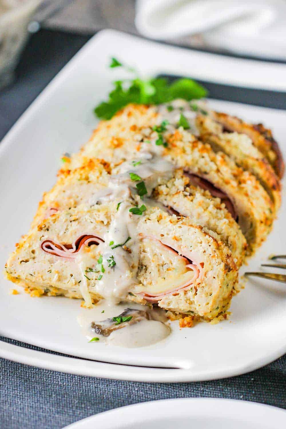 A white platter holding sliced cordon bleu meatloaf with a mushroom gravy drizzled over the top.