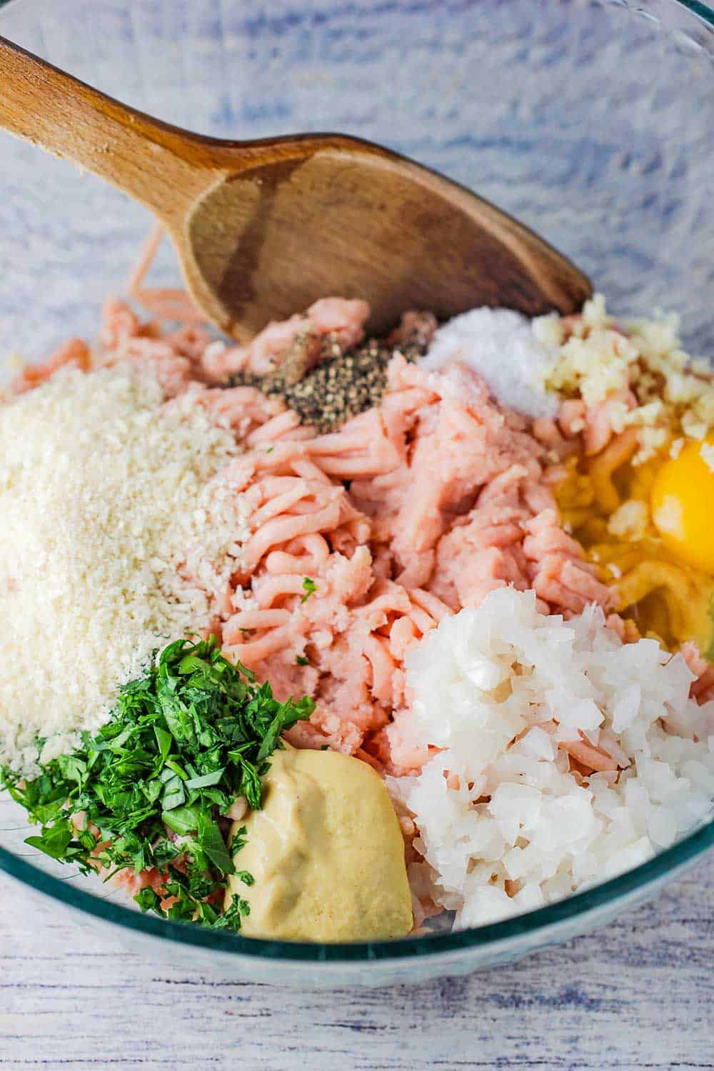 A glass bowl holding the ingredients for cordon bleu meatloaf with a wooden spoon in the bowl.
