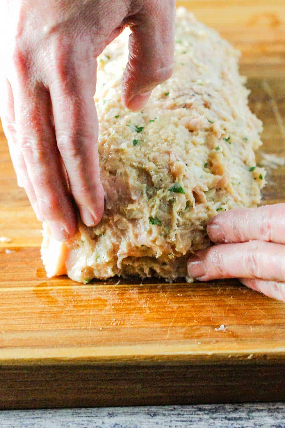 Two hands sealing the end of a chicken cordon bleu meatloaf