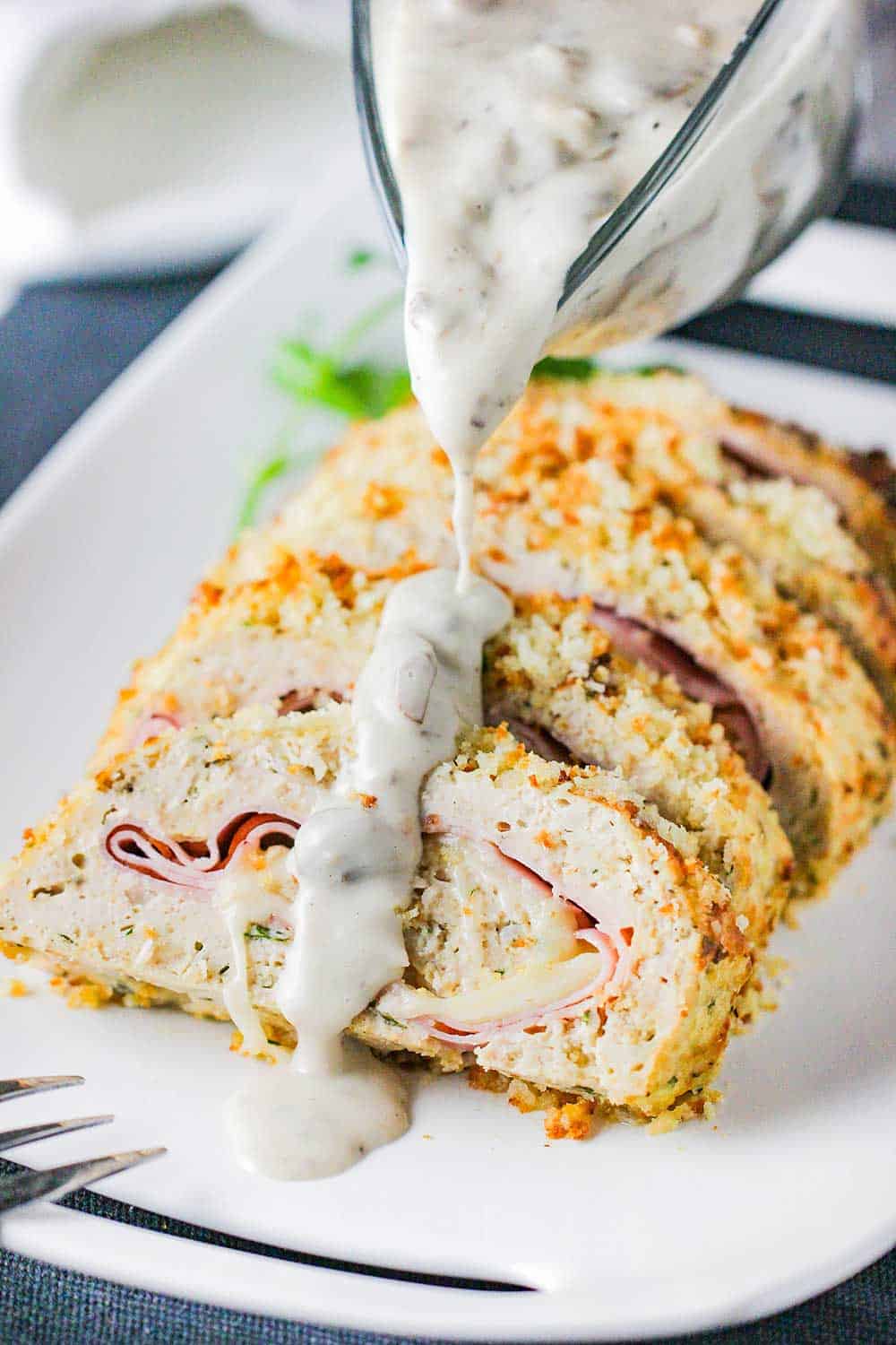 A gravy boat pouring a creamy mushroom sauce over a cordon bleu meatloaf.