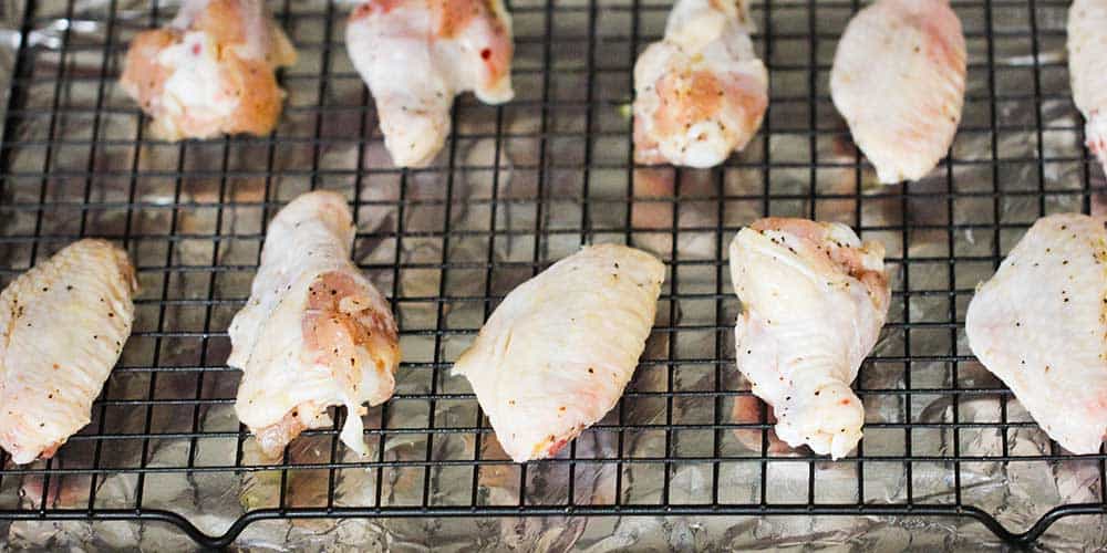 A baking rack in a baking pan topped with uncooked chicken wings.