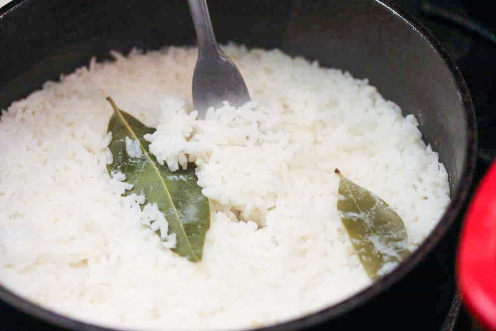 A small saucepan of cooked white rice with 2 bays leaves resting on top.