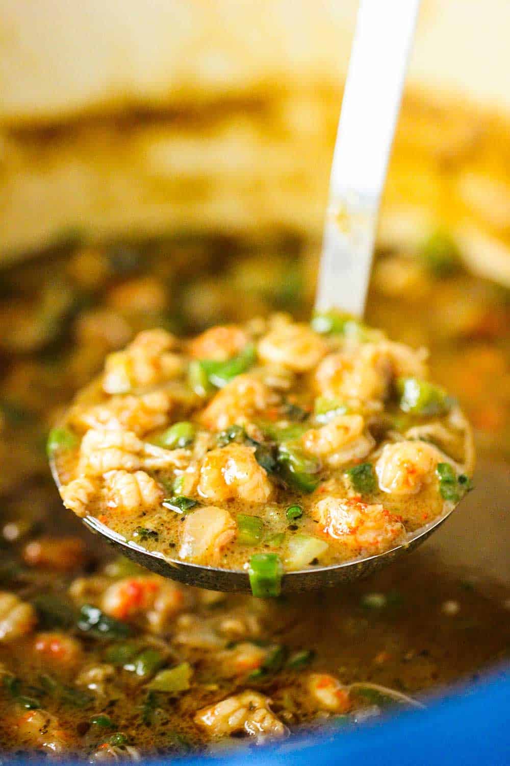 A large wooden spoon stirring cooked crawfish in a cast-iron skillet.