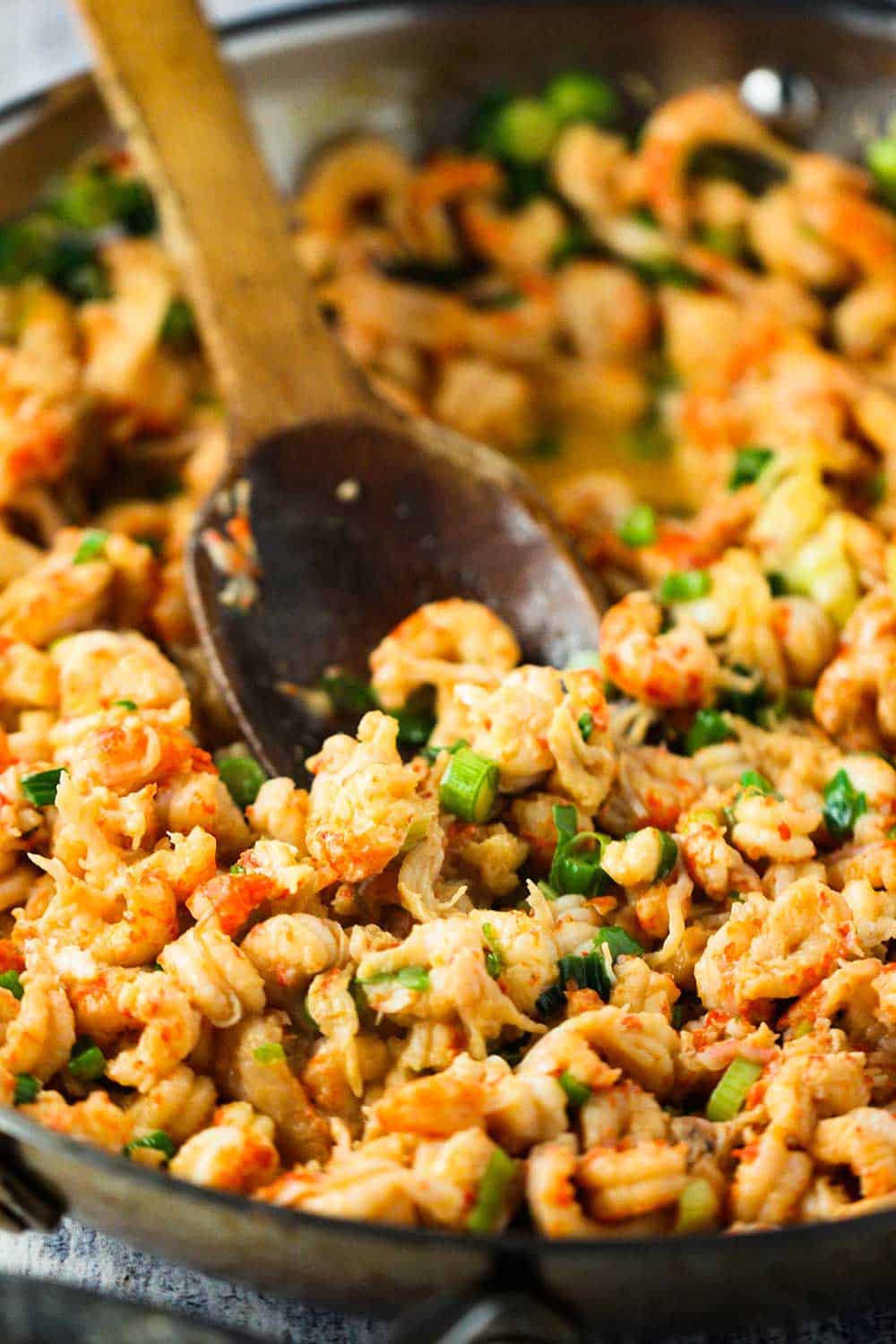 A large wooden spoon stirring cooked crawfish in a cast-iron skillet.