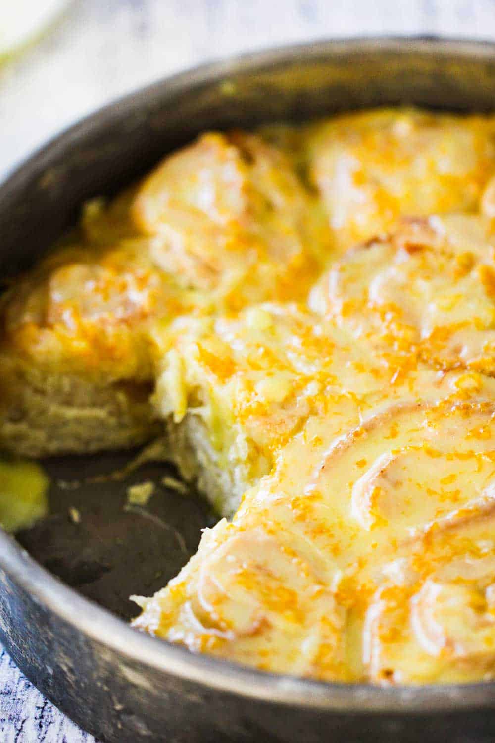 A metal pan holding homemade orange sweet rolls with two rolls missing.