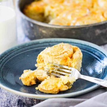 A individual orange sweet roll on a blue plate with a fork cutting it in half.