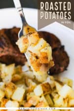 A fork holding up a helping of roasted potatoes in foil over a plate with a grilled steak on it.