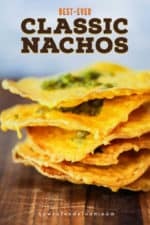 A stack of thin classic nachos topped with jalapeno relish on a wooden cutting board.