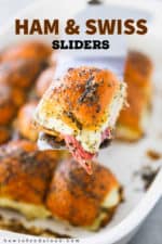A spatula holding up a ham and Swiss slider over a baking dish filled with them.