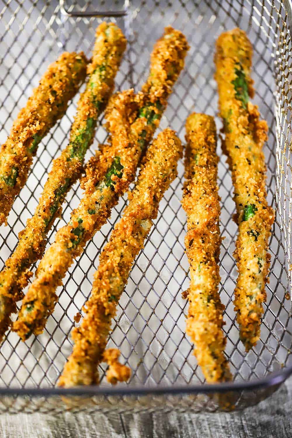 A fryer basket holding a batch of fried asparagus.