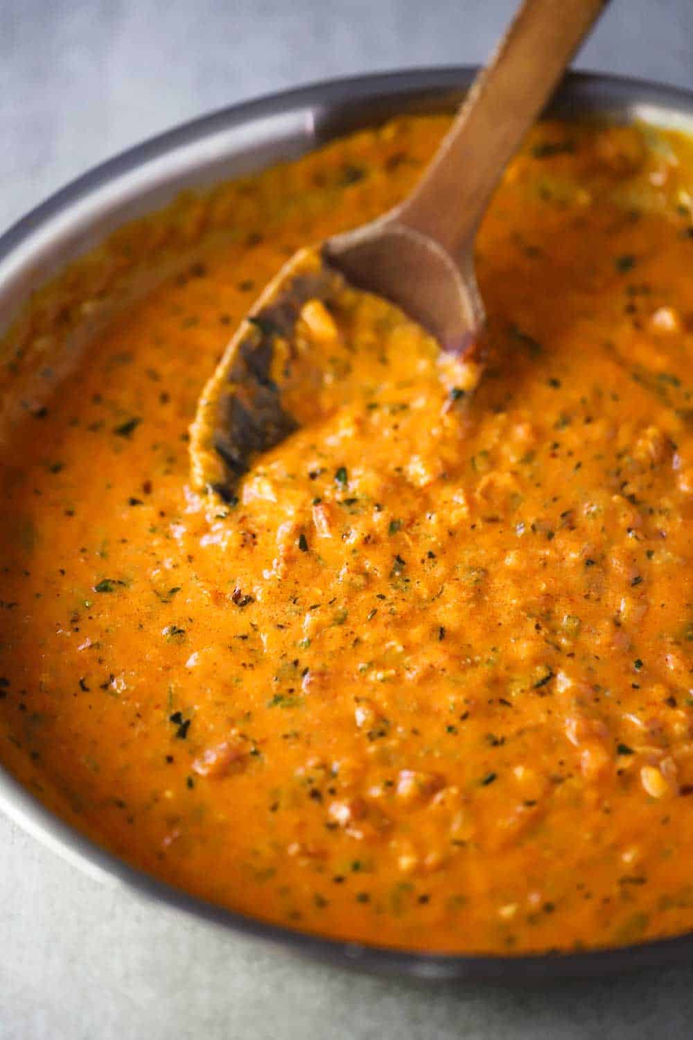 A skillet filled with a Italian vodka sauce with a wooden spoon in it.