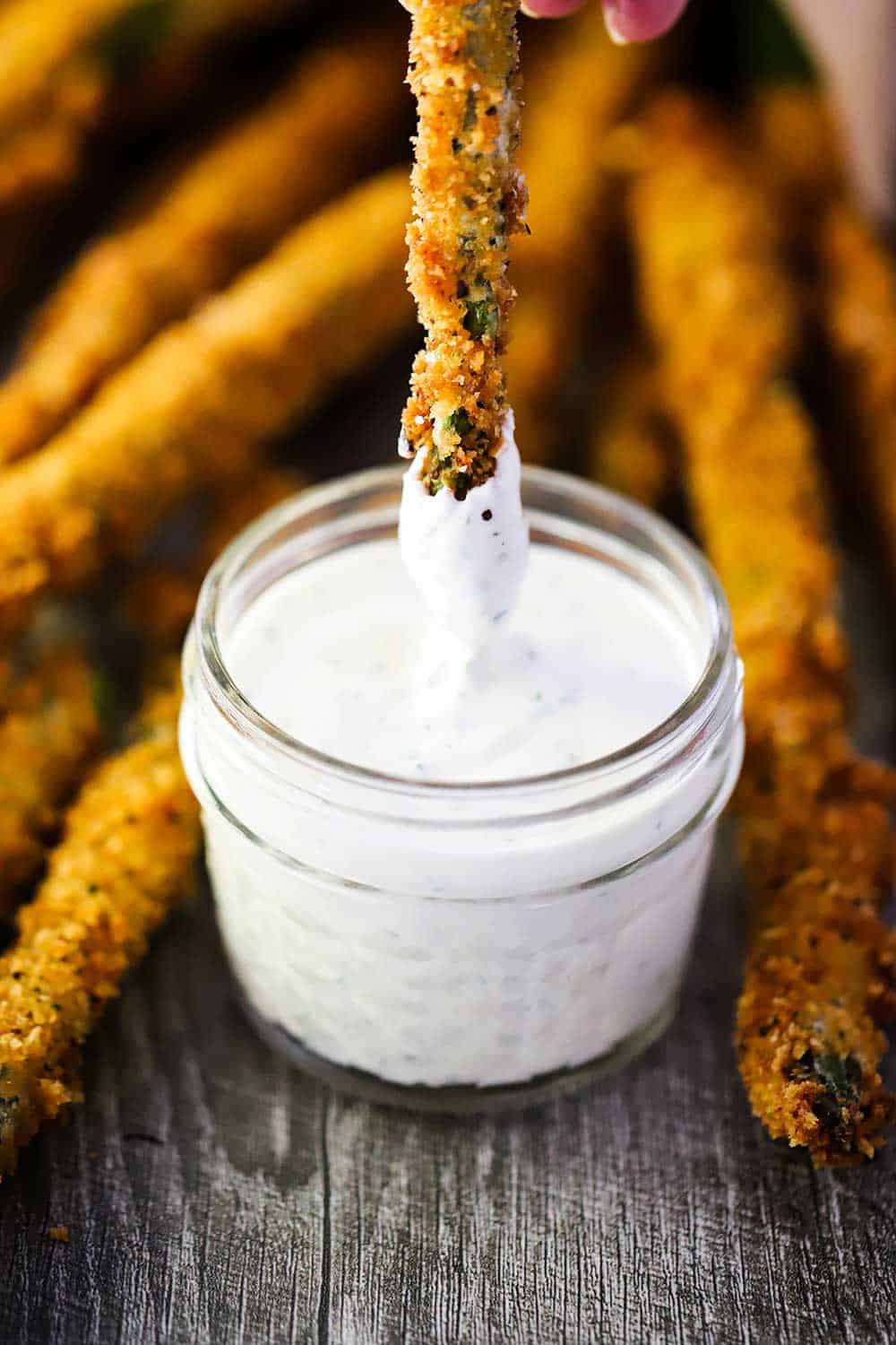 The tip of a fried asparagus being dipped into a small jar of homemade ranch dressing.
