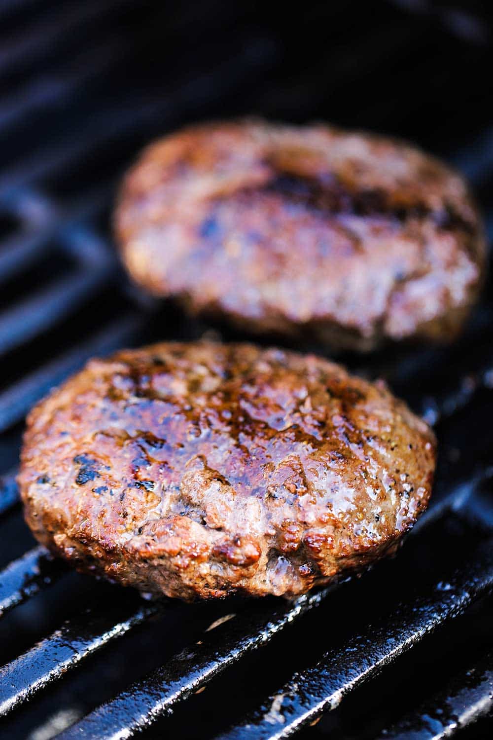 Two hamburger patties on a grill being cooked for mushroom Swiss burgers.