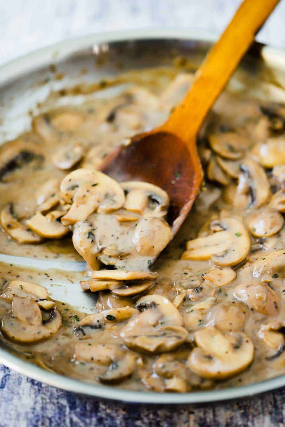 A large skillet filled with a mushroom sauce with a wooden spoon in it.