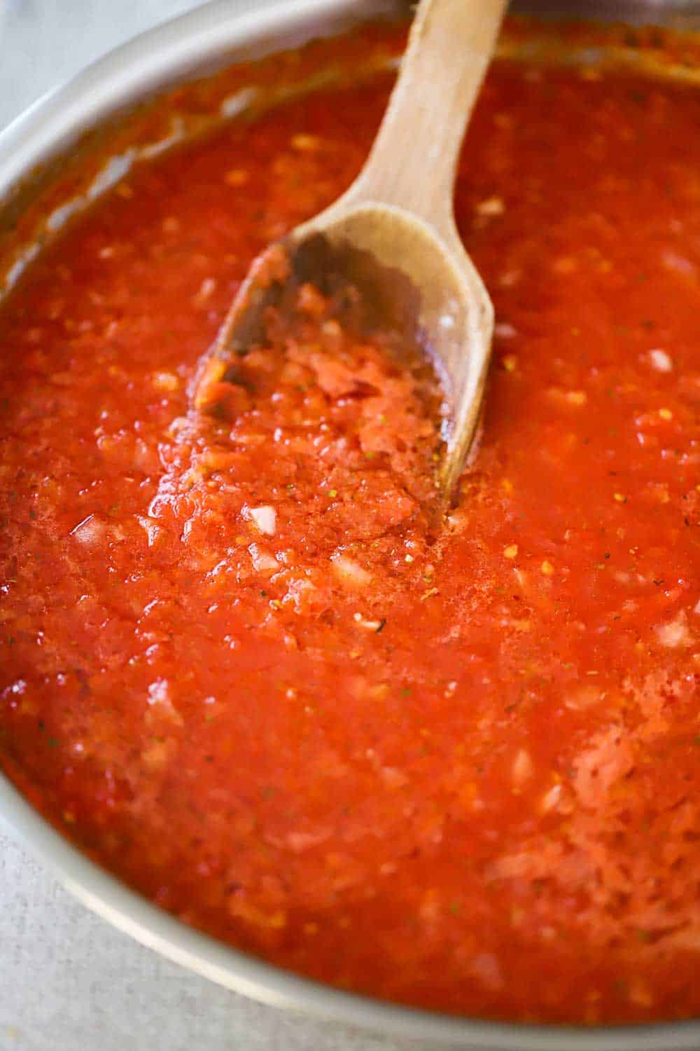 A large silver skillet filled with a red sauce with a wooden spoon in it.