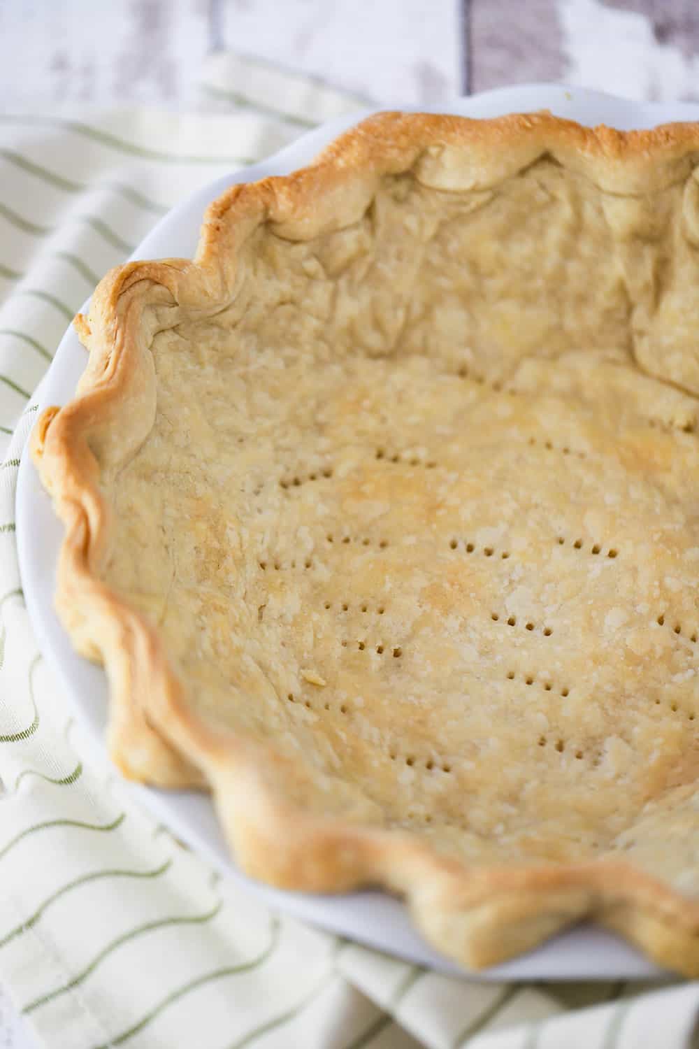 An overhead view of a baked pie shell in a white pie dish with fork holes throughout the base of the shell.