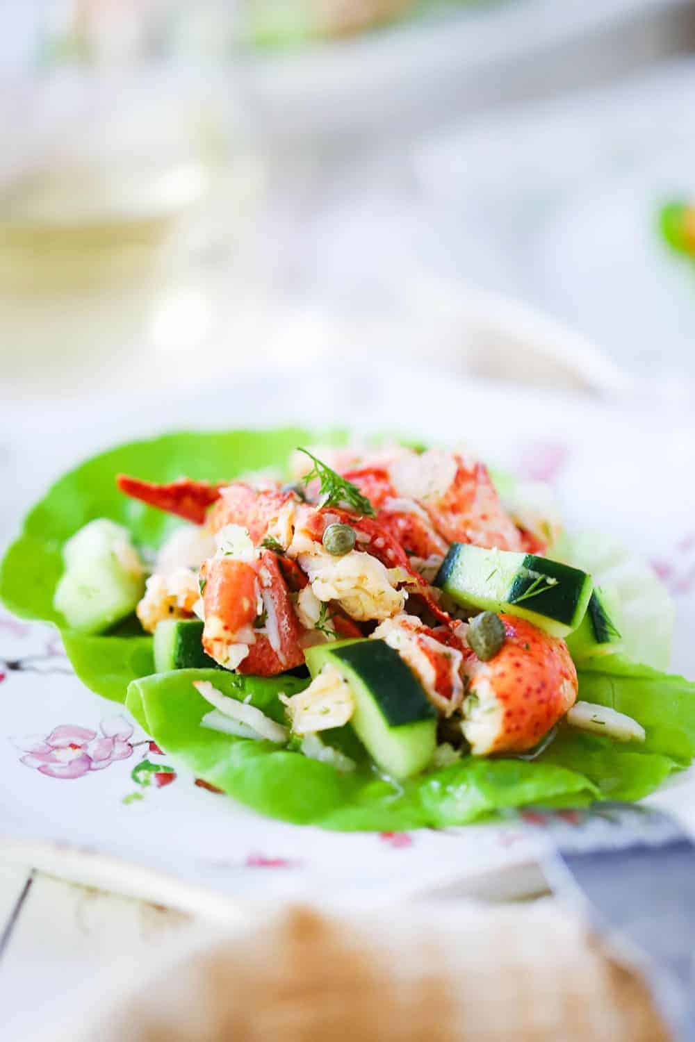 A close-up view of a lobster salad with cucumbers on a green leaf of lettuce on a decorative plate.