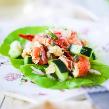 A close-up view of a lobster salad with cucumbers on a green leaf of lettuce on a decorative plate.