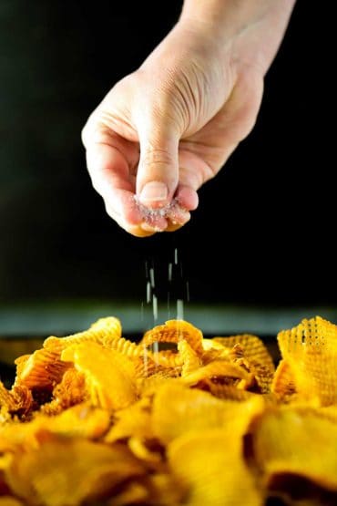 A hand sprinkling coarse sea salt over freshly made cross hatch sweet potato chips.